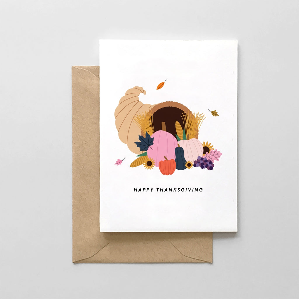 White card with black text saying, "Happy Thanksgiving". Images of a Thanksgiving cornucopia with fruits and vegetables. A brown envelope is included.