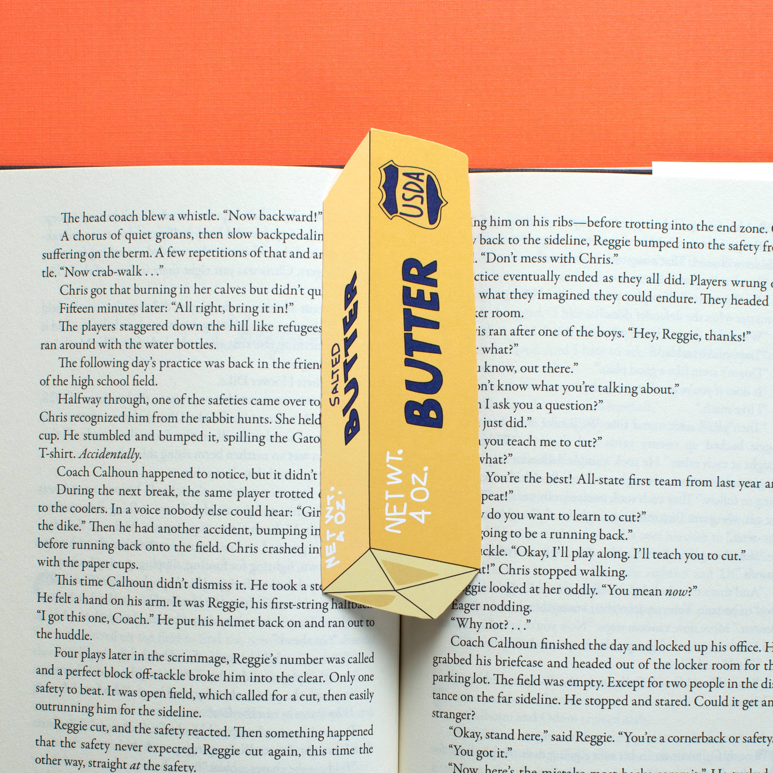 Image of opened book with bookmark in the shape of a yellow stick of butter with blue text says “Butter” and USDA symbol. .
