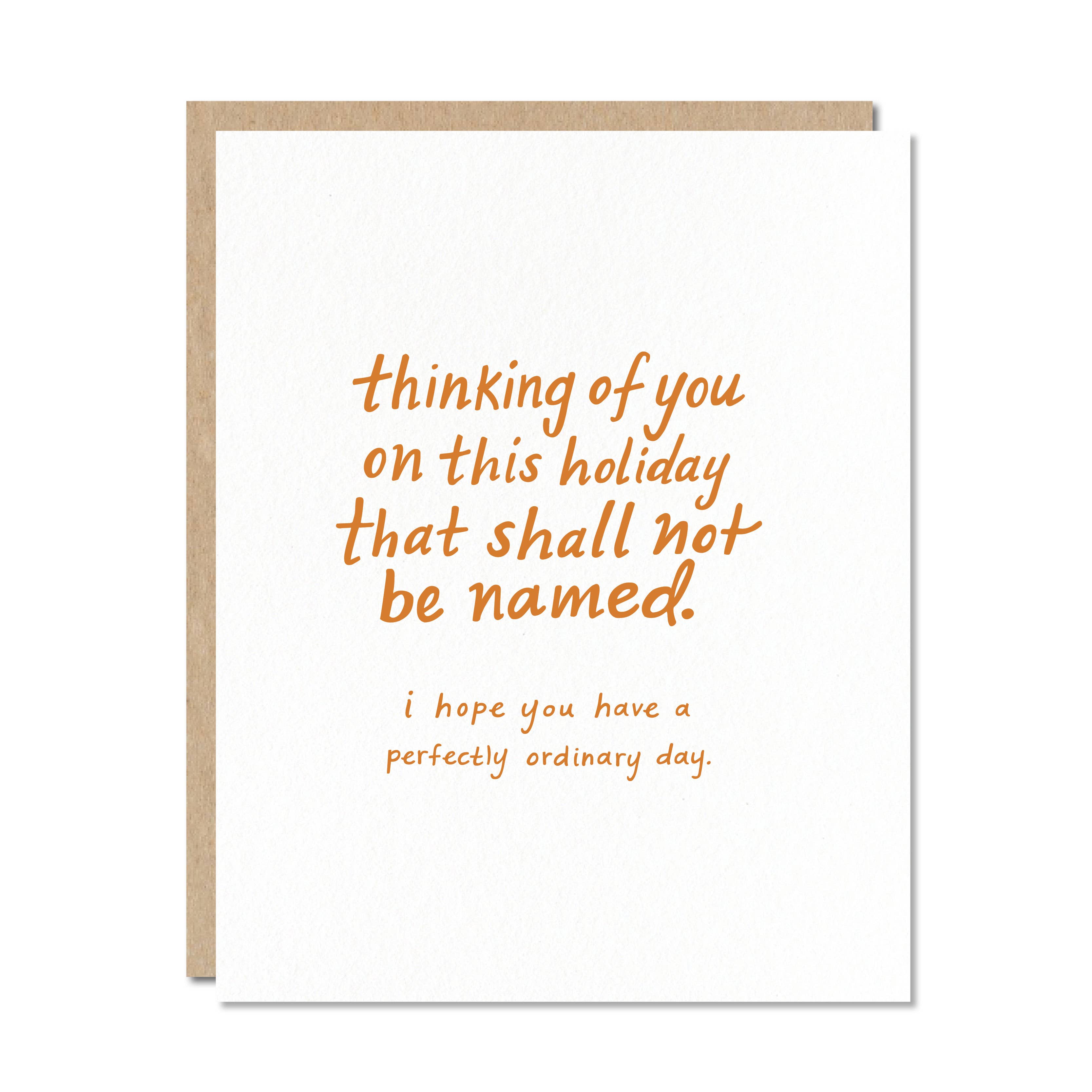 White card with orange text saying, "Thinking of You on This Holiday That Shall Not Be Named. I Hope You Have a Perfectly Ordinary Day".  A brown envelope is included.