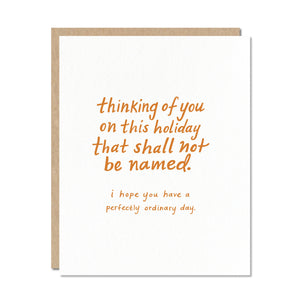 White card with orange text saying, "Thinking of You on This Holiday That Shall Not Be Named. I Hope You Have a Perfectly Ordinary Day".  A brown envelope is included.