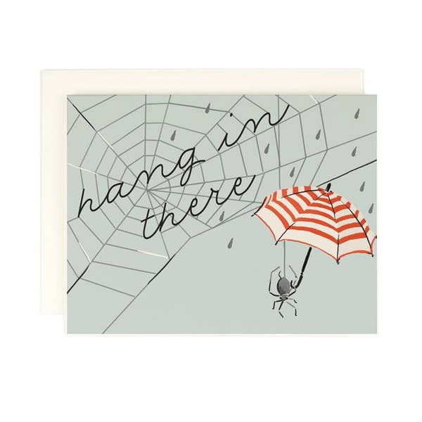 Grey background with image of a dark grey spider holding a red and white stripe umbrella. Image of a spider web in dark grey with black text says, “Hang in there”.  A white envelope is included.       