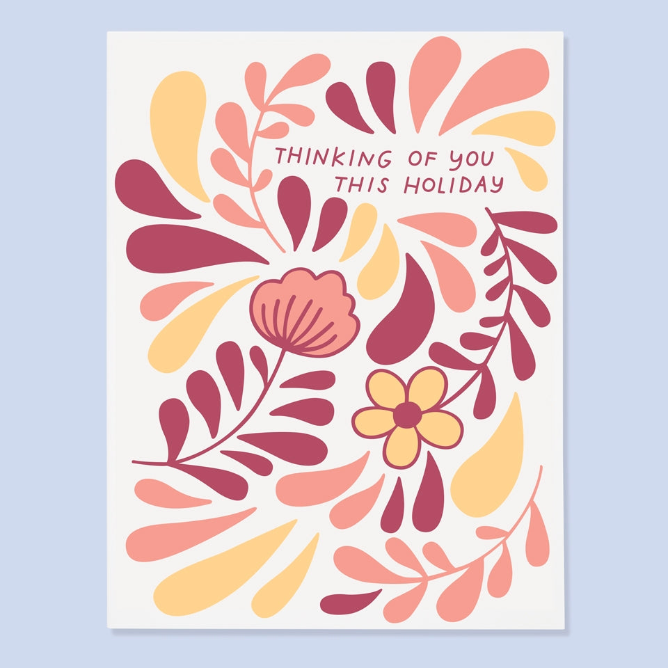 White card with pink text saying, “Thinking of You This Holiday”. Images of pink and yellow flowers and petals. An envelope is included.