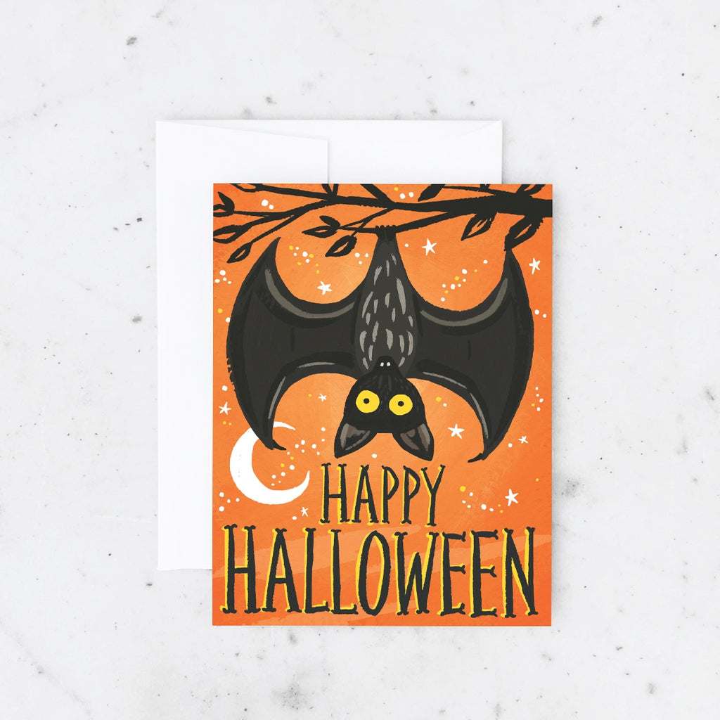 Orange card with black and yellow text saying, “Happy Halloween”. Images of a black bat hanging upside down from a tree branch with a white moon and white stars. A white envelope is included.