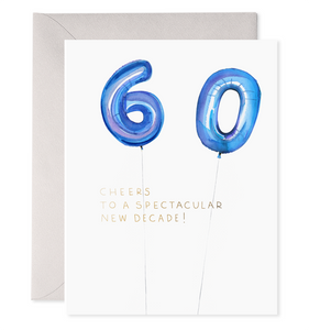 White card with black text saying, “Cheers to A Spectacular Decade”.  Images of blue foil balloons in the shape of a six and a zero. A purple envelope is included.