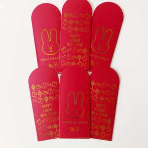 Image of red envelopes with gold foil images of rabbit and other Lunar New Year treats with goil foil text says, “Year of the Rabbit” and Chinese characters. 