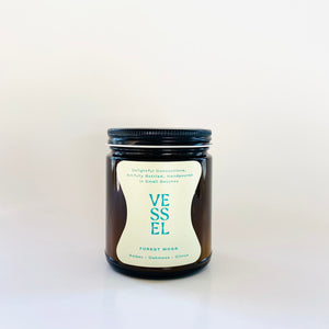 Image of brown glass jar with black lid and ivory label with teal text says, “Vessel” and “Forest Moss”. 