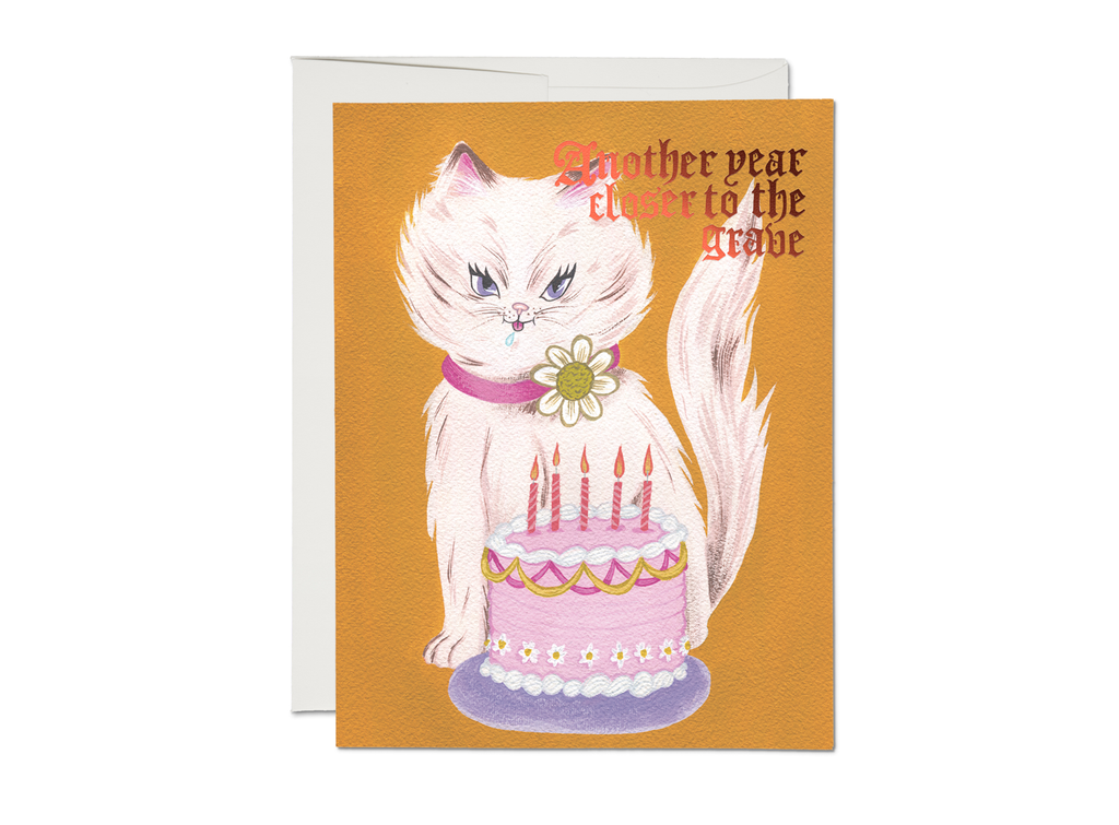 Orange card with red foil text saying, “Another Year Closer to the Grave”. Images of a white cat wearing a pink collar with a white daisy on it, sitting in front of a pink birthday cake with pink candles. A white envelope is included.