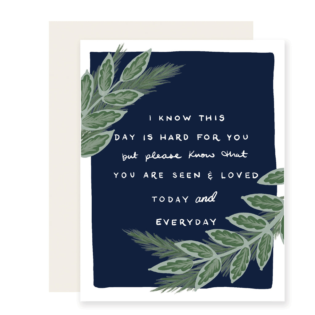 Blue card with white text saying, “I know this day is hard for you but please know that you are seen and loved today and everyday”. Images of green fern leaves in corners of card. A white envelope is included.