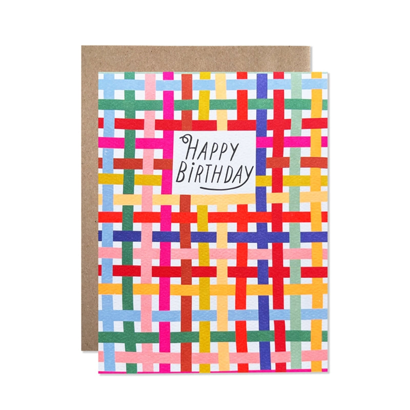 White card with black text saying, “Happy Birthday”. Images of multi colored lines in a woven pattern. A brown envelope is included.