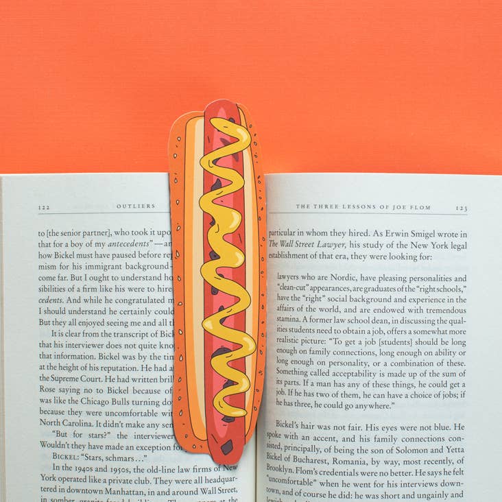 Image of opened book with bookmark in the shape of a brown hotdog on a yellow bun with a drizzle of yellow mustard.