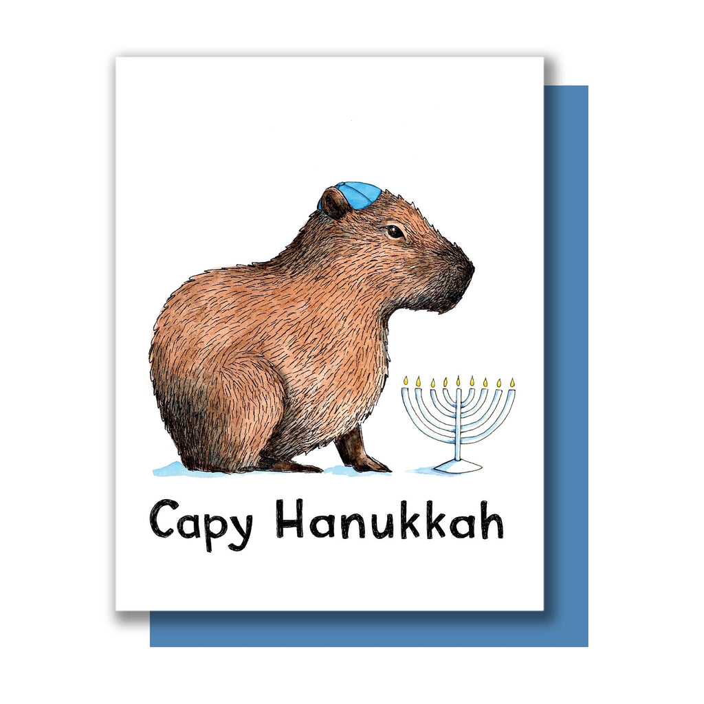White card with black text saying, “Capy Hanukkah”. Image of a capybara wearing a blue yamaka. White menorah with yellow flames in background. A blue envelope is included.