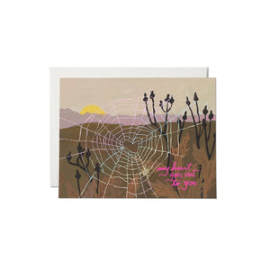 Card with a desert scene with plants, mountains and sunset with a spiderweb in the foreground. Pink text saying, “My Heart Goes Out to You”. A white envelope is included.