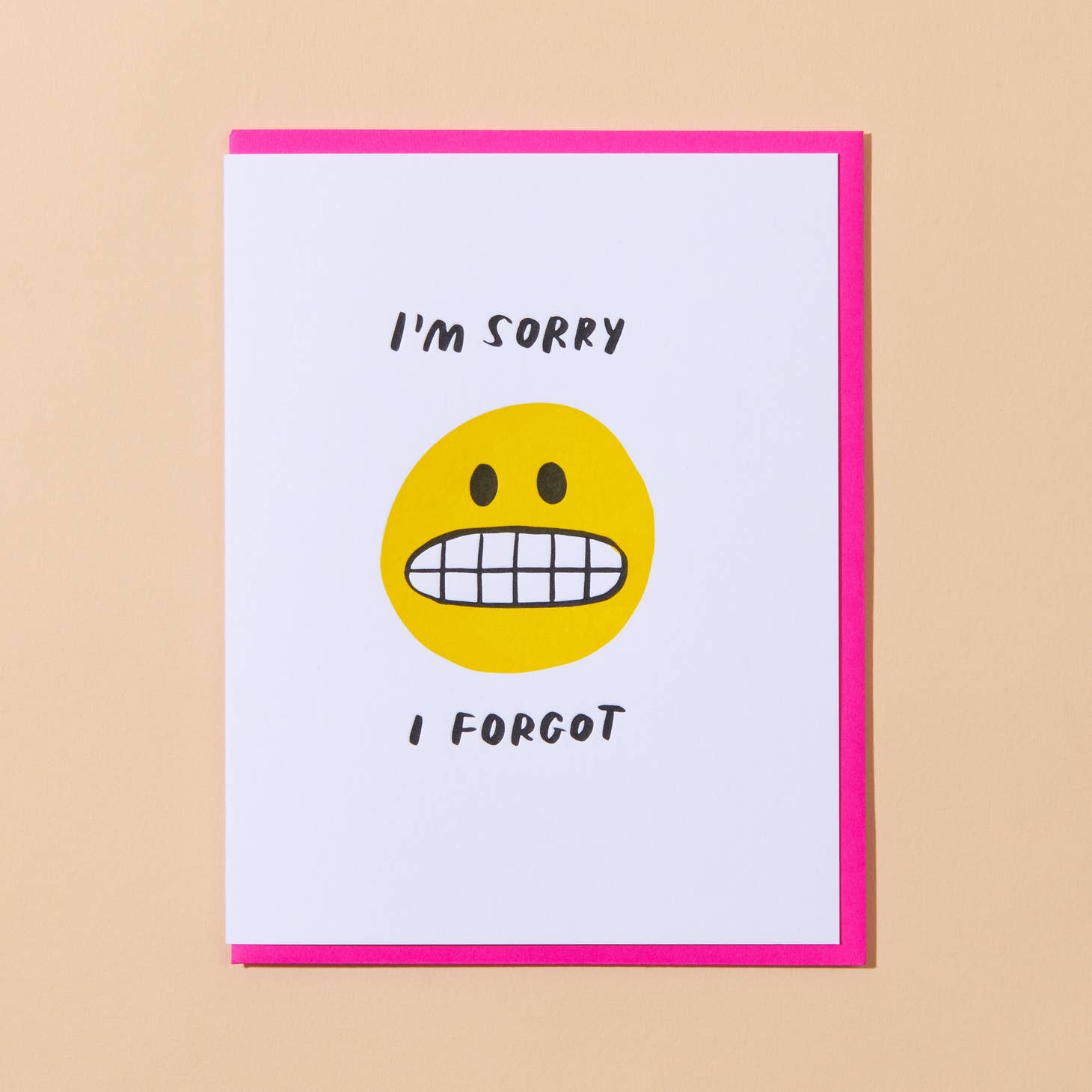 White card with yellow image of smiling face with toothy grin saying “I’m sorry" and "I forgot” in black text. Hot pink envelope included.     