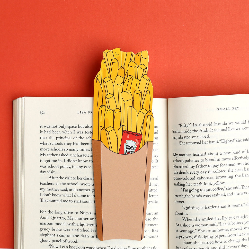 Image of opened book with bookmark in the shape of a container of French fries with  a packet of ketchup peeking out.. 