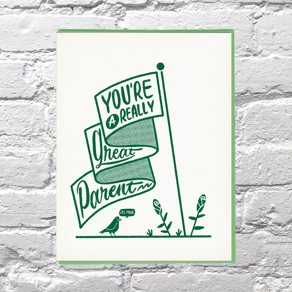 Ivory card with green text saying, “You’re A Really Great Parent It’s True”. Image of a ribbon flag with green flowers and a green bird. A green envelope is included.