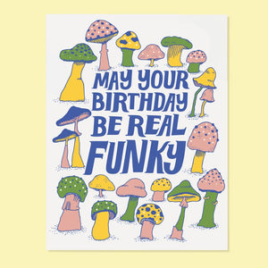 White card with blue text saying, “May Your Birthday Be Real Funky”. Images of multi colored mushrooms. An envelope is included.