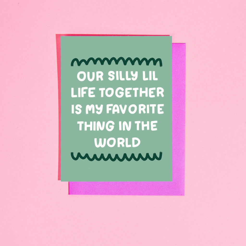 Green background with white text says, “Our silly lil life together is my favorite thing in the world”. A bright pink envelope is included.       