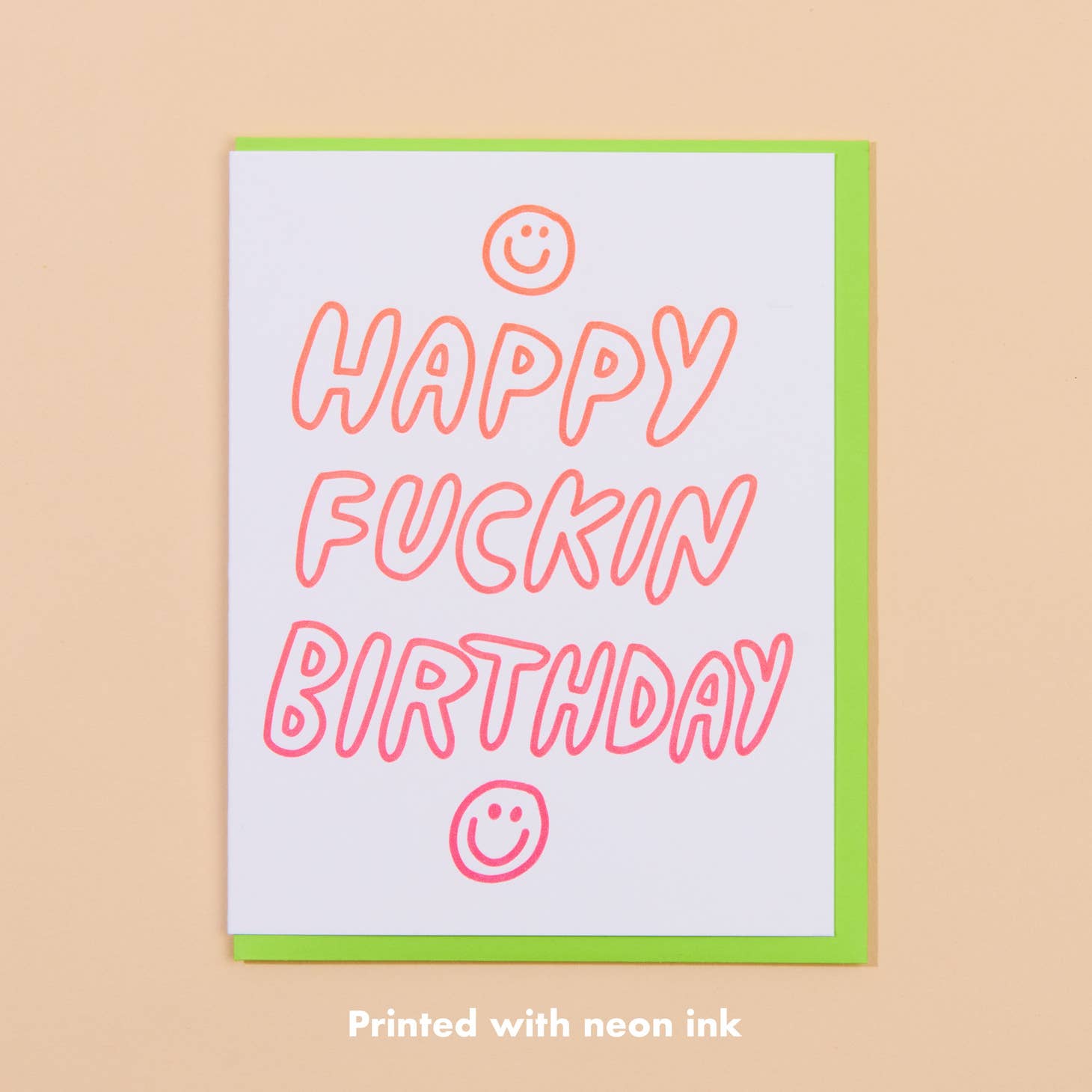White card with orange ombre text saying “Happy Fuckin Birthday” with two images of smiling face emojis. Bright green envelope included.   