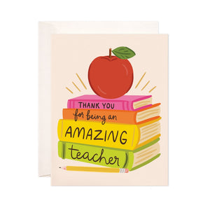 Cream card with black text saying, “Thank You for Being An Amazing Teacher”. Images of an apple sitting on a stack of books. A white envelope is included.