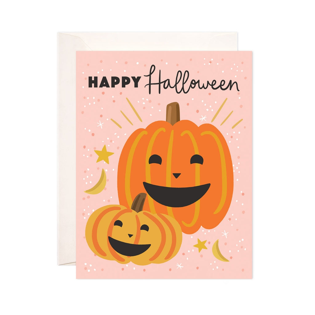 Pink card with black text saying, "Happy Halloween". Image of two smiling orange pumpkins and gold stars. An ivory envelope is included.
