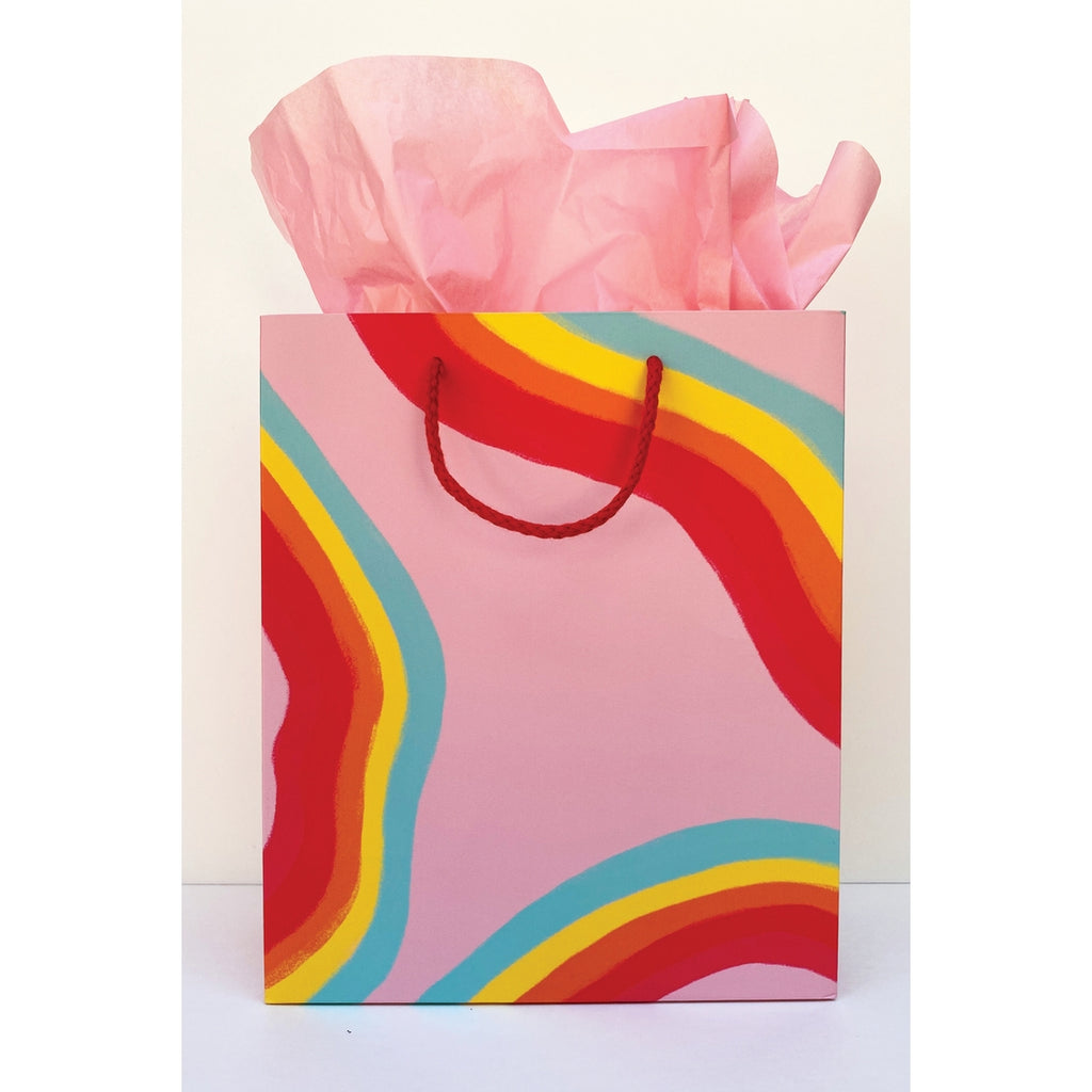Pink gift bag with red, orange, yellow, and teal wavy rainbows and red rope handle, 