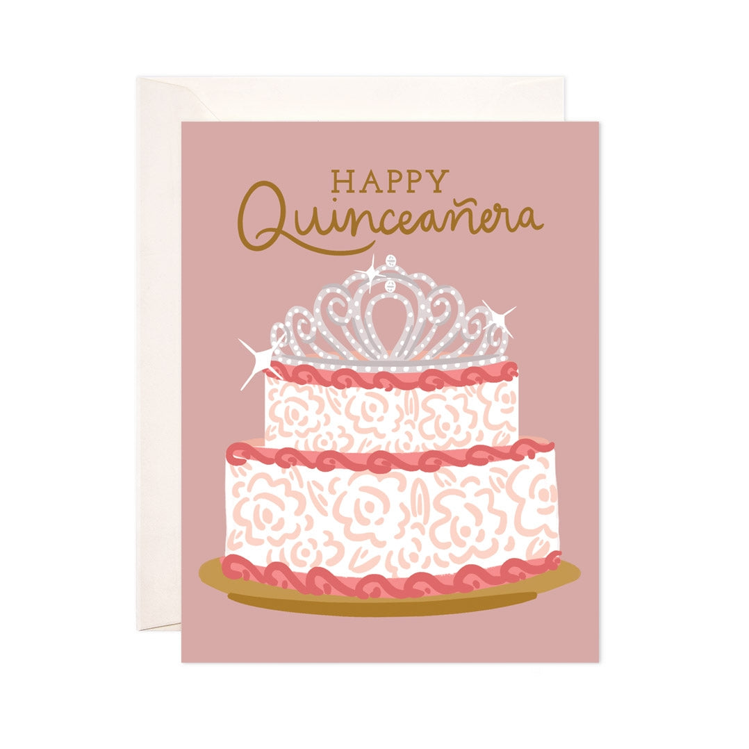 Mauve card with gold text saying, "Happy Quinceanera". Image of a white cake with pink frosting and jeweled tiara on top. An ivory envelope is included.