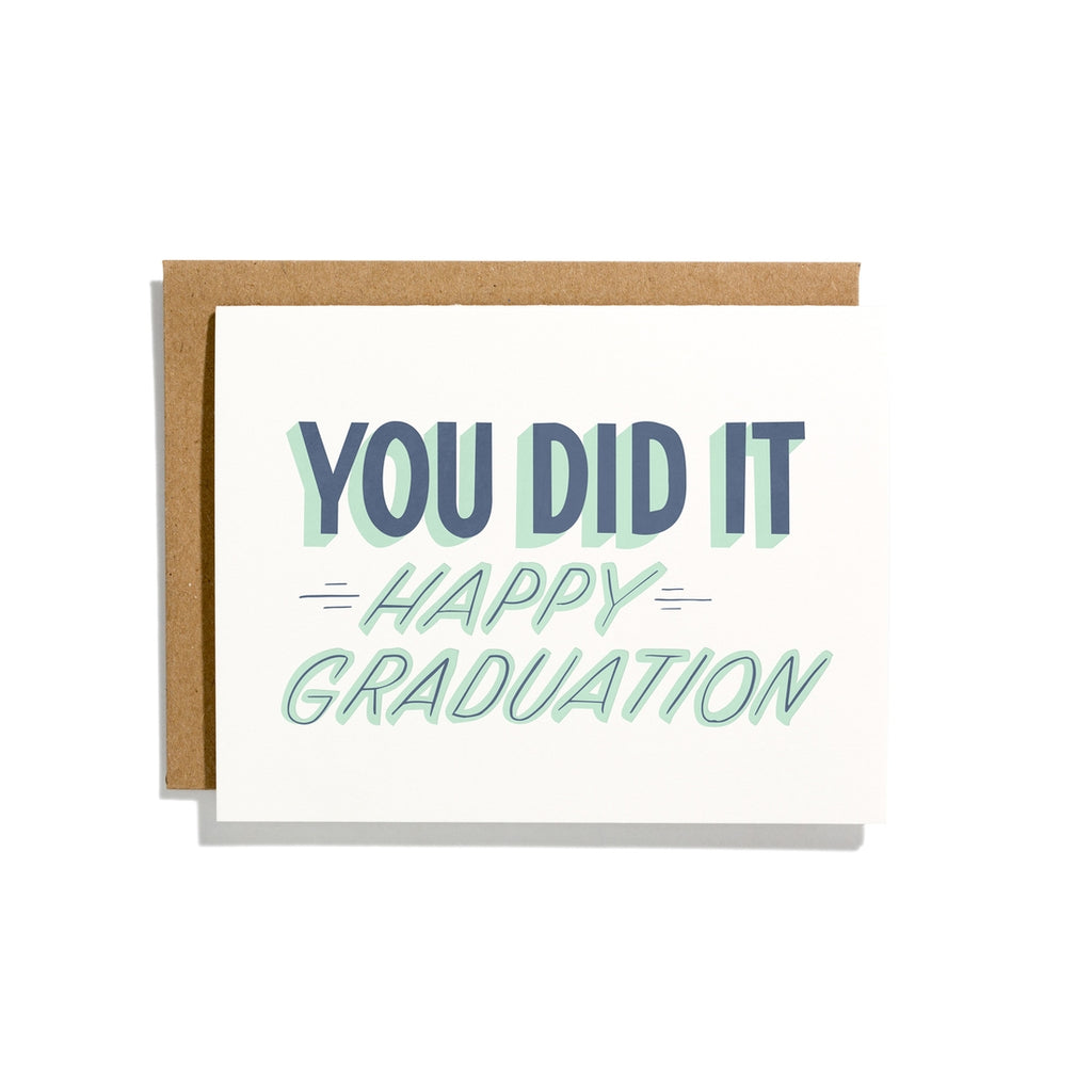 White card with blue and teal shadow text saying, “You Did It Happy Graduation”. A brown envelope is included.