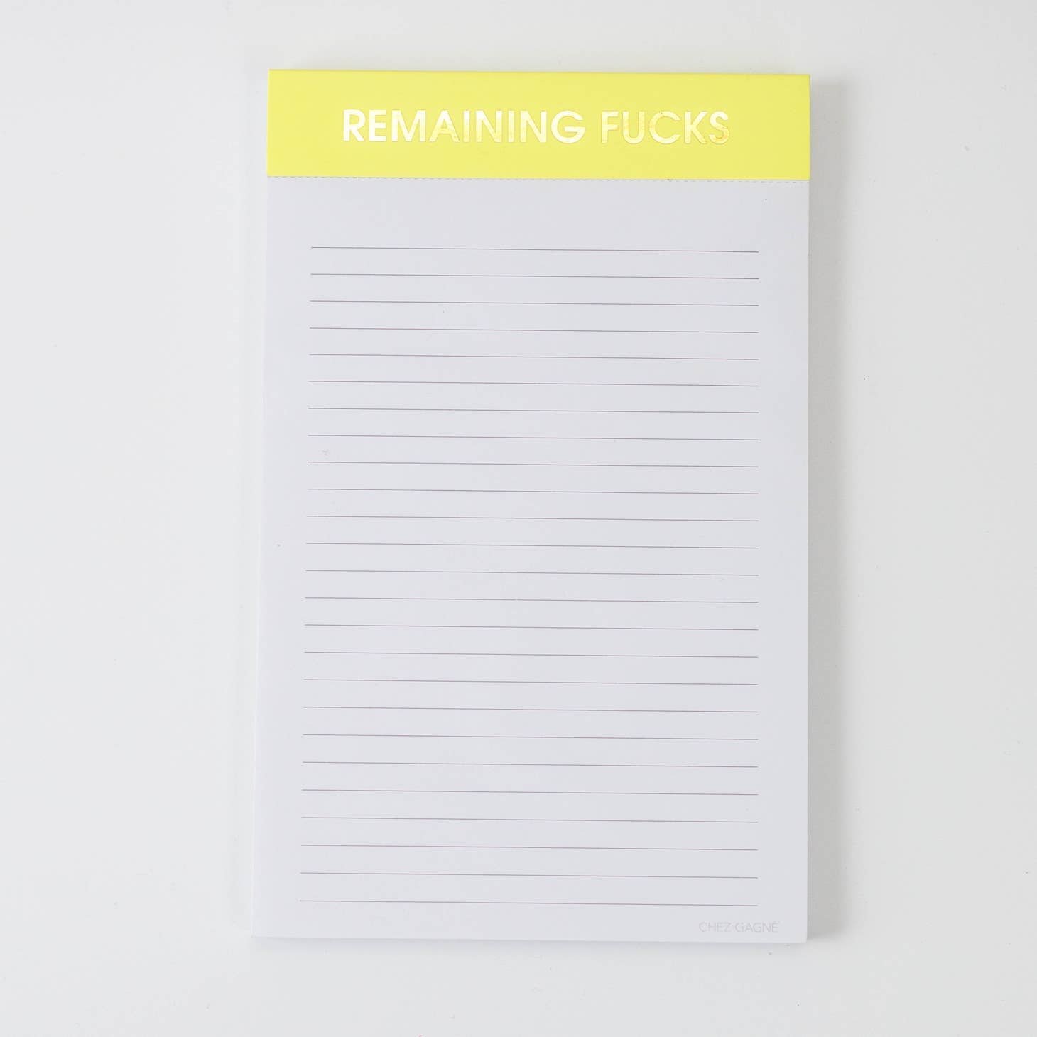 Image of a notepad with white lined paper and yellow binding with gold foil text says, “Remaining fucks”. 