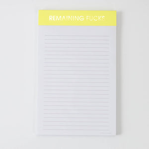 Image of a notepad with white lined paper and yellow binding with gold foil text says, “Remaining fucks”. 