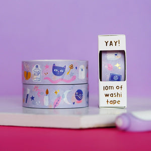 Decorative tape with light purple background with images of various halloween items such as blue cats, white ghosts, white moons, white candles, gold keys, pinlk leaves and pink stars.