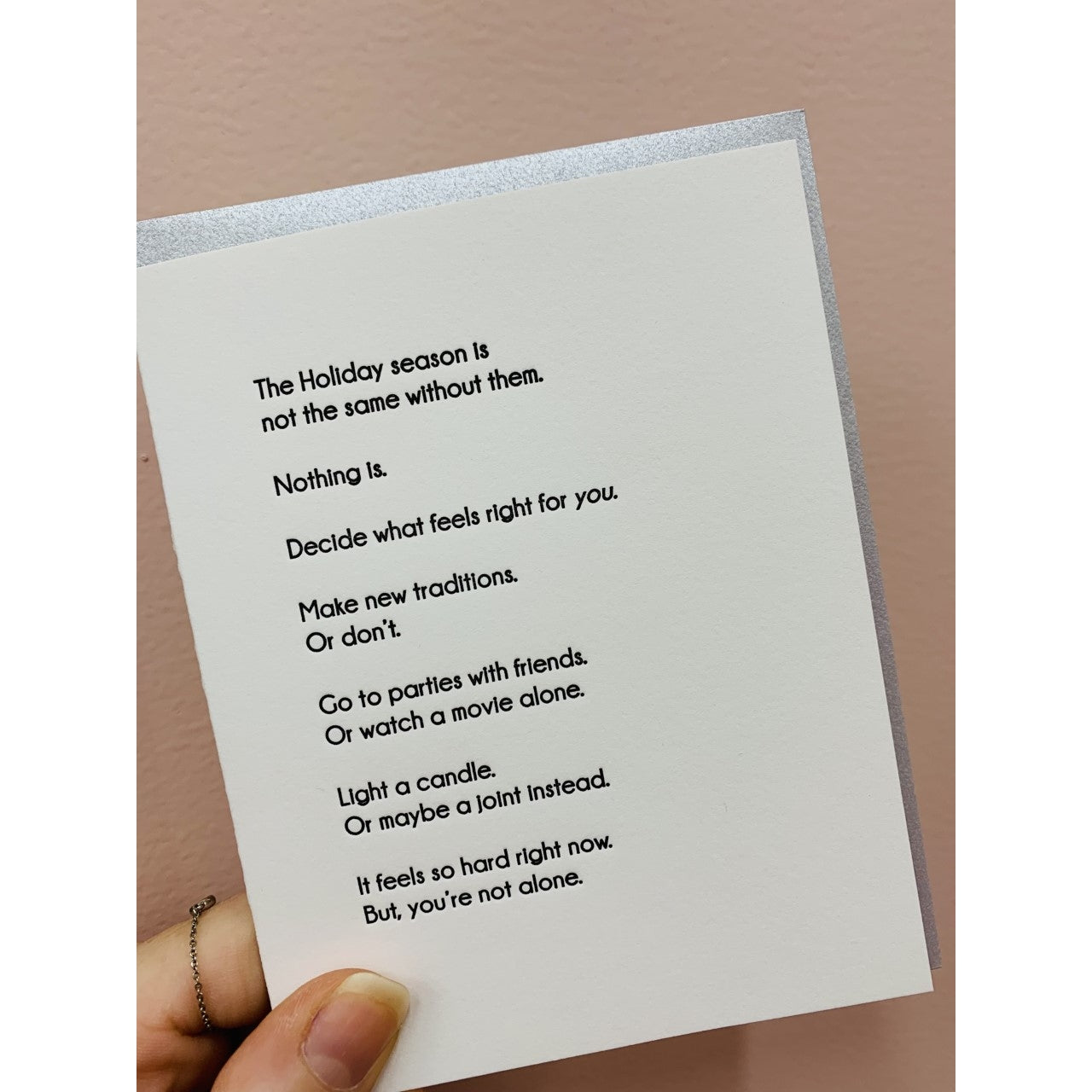Ivory card with black text saying, "The Holiday season is not the same without them. Nothing is. Decide what feels right for you. Make new traditions. Or don't. Go to parties with friends. Or watch a movie alone. Light a candle. Or maybe a joint instead. It feels so hard right now. But, you're not alone."  A gray envelope is included.