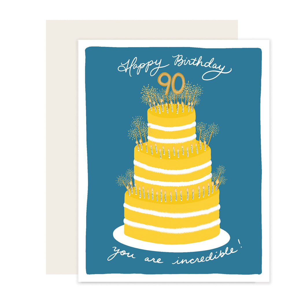 Blue card with white text saying, “Happy Birthday You Are Inspiring”. Images of a three tier yellow birthday cake with white and gold candles and an 90 gold cake topper. An ivory envelope is included.