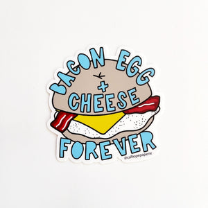 Image of bacon, egg and cheese sandwich on a tan bagel with blue text says, “Bacon egg + cheese forever”,  