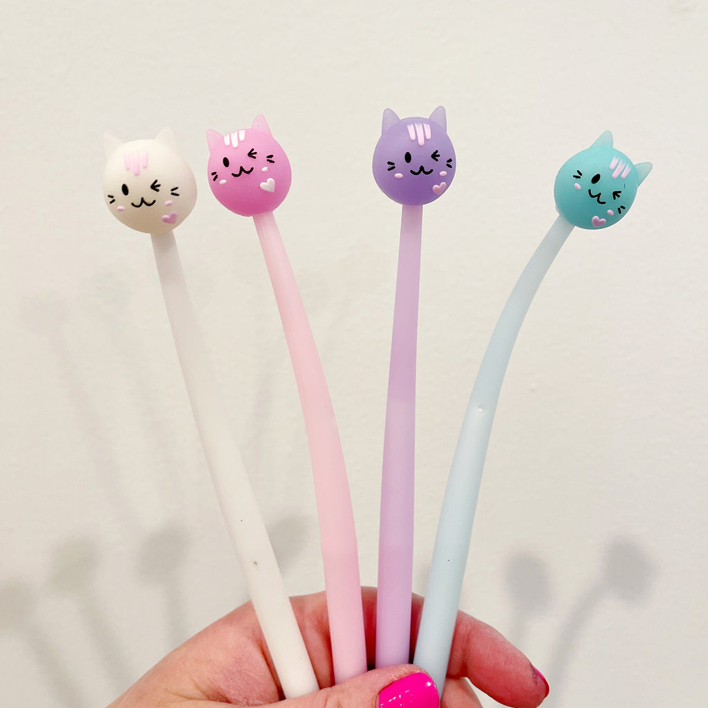 Image of four pens with cat heads on top of the barrel. White cat with facial features in black with white barrel, pink cat with facial features in black with pink barrel, lilac cat with facial features in black with lilac barrel and blue cat with facial features in black with blue barrel.        