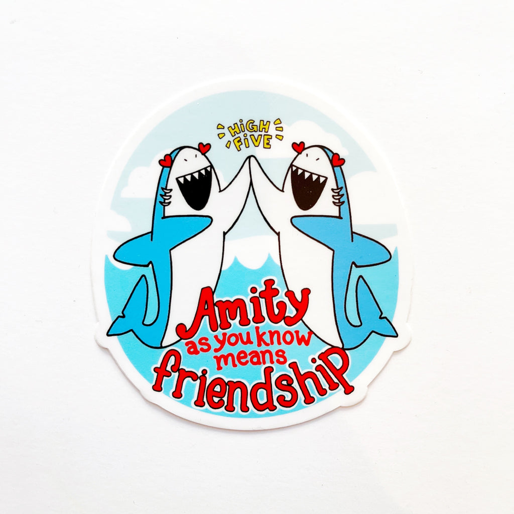 Image of two blue sharks with white underbelly and red heart shaped eyes high fiving with their fins. Background of blue ocean and sky with white clouds. Yellow text says, “High five” and red text says, “Amity as you know means friendship”. 
