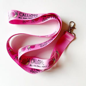 image of bright pink lanyard with silver clip and black text says, "Calliope all hail snail mail" and images of Ernie the snail. 