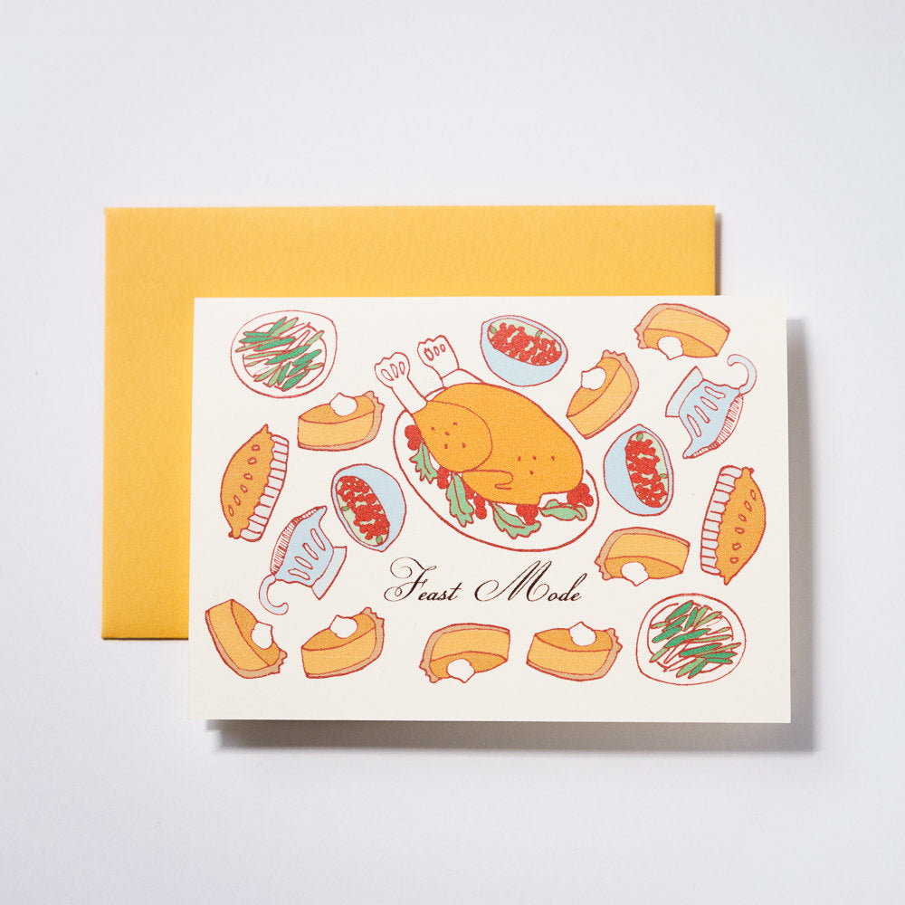 Ivory card with black text saying, “Feast Mode”. Images of foods from a Thanksgiving feast. A yellow envelope is included.
