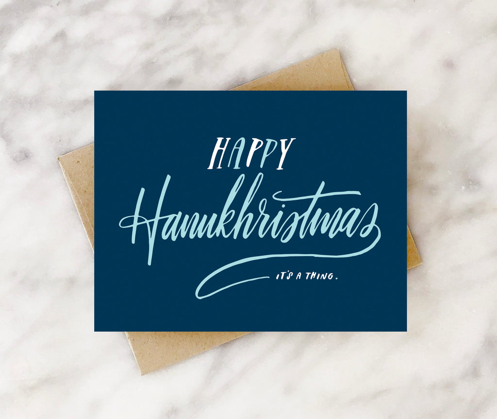 Dark blue card with light blue text saying, “Happy Hanukhristmas It’s a Thing”. A brown envelope is included.