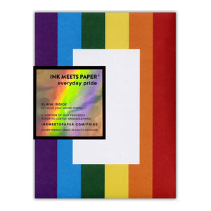 White card with black text saying, “Here & Queer”. A rainbow striped envelope is included.