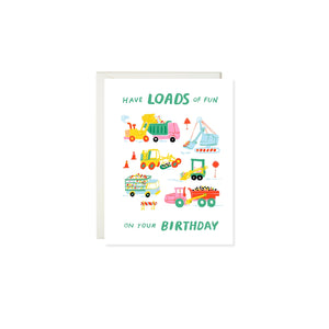 White background with images of various work trucks including a pink and green dump truck, a light blue steam shovel, a yellow and orange front loader, a blue and yellow produce truck and a pink bulldozer. Green text says, “Have loads of fun on your birthday”. A white envelope is included.  