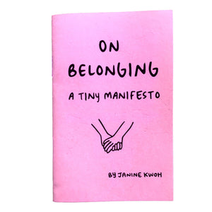 Bright pink background with black text says, “On belonging a tiny manifesto” with image of two holding hands. 