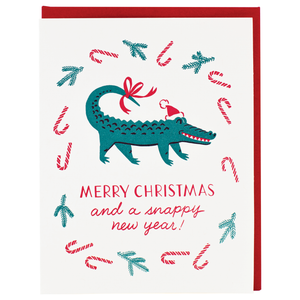 White card with red text saying, “Merry Christmas and  A Snappy New Year!” Images of a green alligator wearing a Santa hat. Candy canes and sprigs of pine branches floating in background. A red envelope is included.