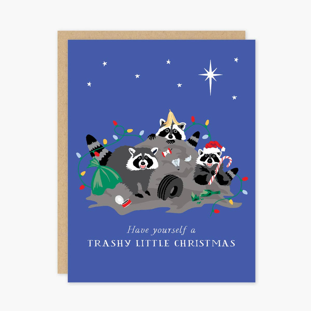 Blue card with white text saying, “Have Yourself A Trashy Little Christmas”. Images of three raccoons hanging out on top of a trash heap. Candy canes, Christmas lights, and Santa hats on trash heap. White stars above. A brown envelope is included.