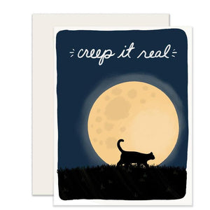 Navy blue card with white text saying, “Creep It Real”. Images of night sky with big yellow full moon in background and black cat walking on the grass in front of moon. A white envelope is included. 