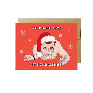 Red card with white text saying, “Yippie-Ki-Yay! It’s Christmas”. Image of the character, John McLane form the Die Hard movie in center of card. A brown envelope is included.