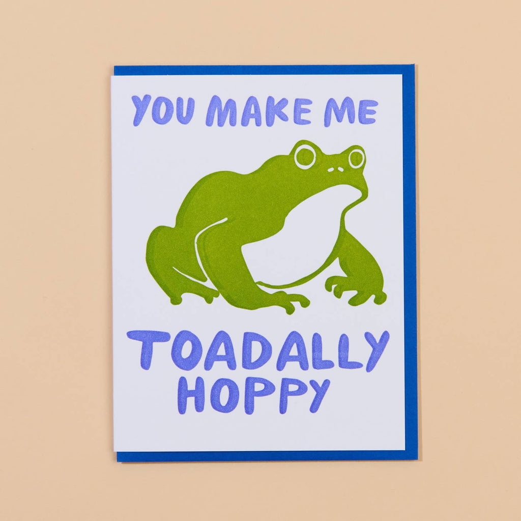 White card with image of a green toad and blue text that says “You make me toadally hoppy”. Blue envelope included.        