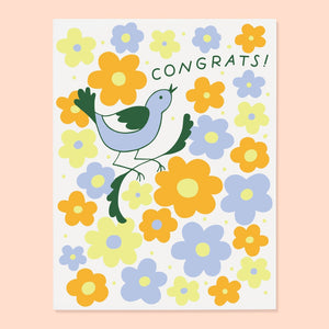 White card with green text saying, “Congrats!” Images of a bluebird sitting on a branch with blue and yellow flowers scattered on card. An envelope is included.