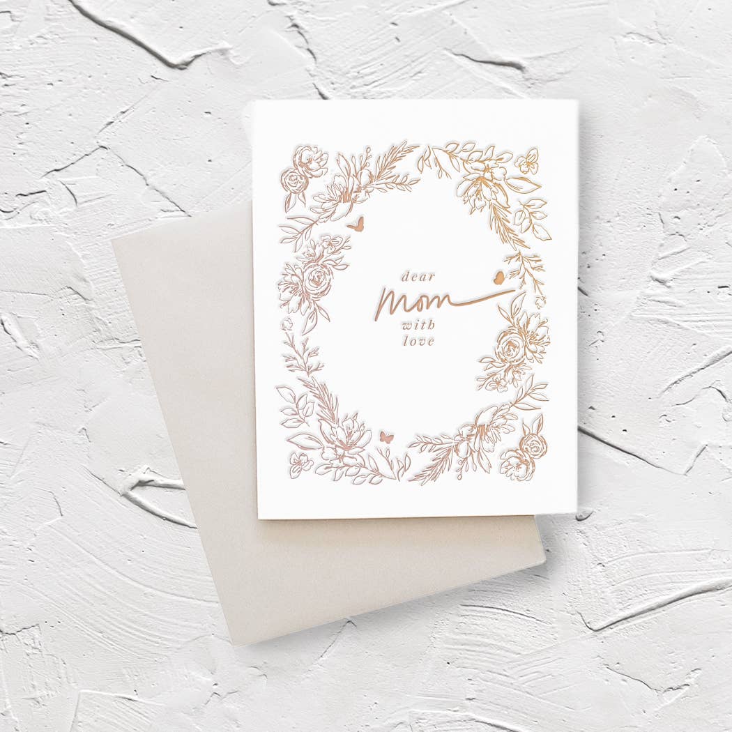 Ivory background with tan images of flowers, leaves and butterflies. Text in middle says in tan says, “Dear Mom with love”. A silver envelope is included.   