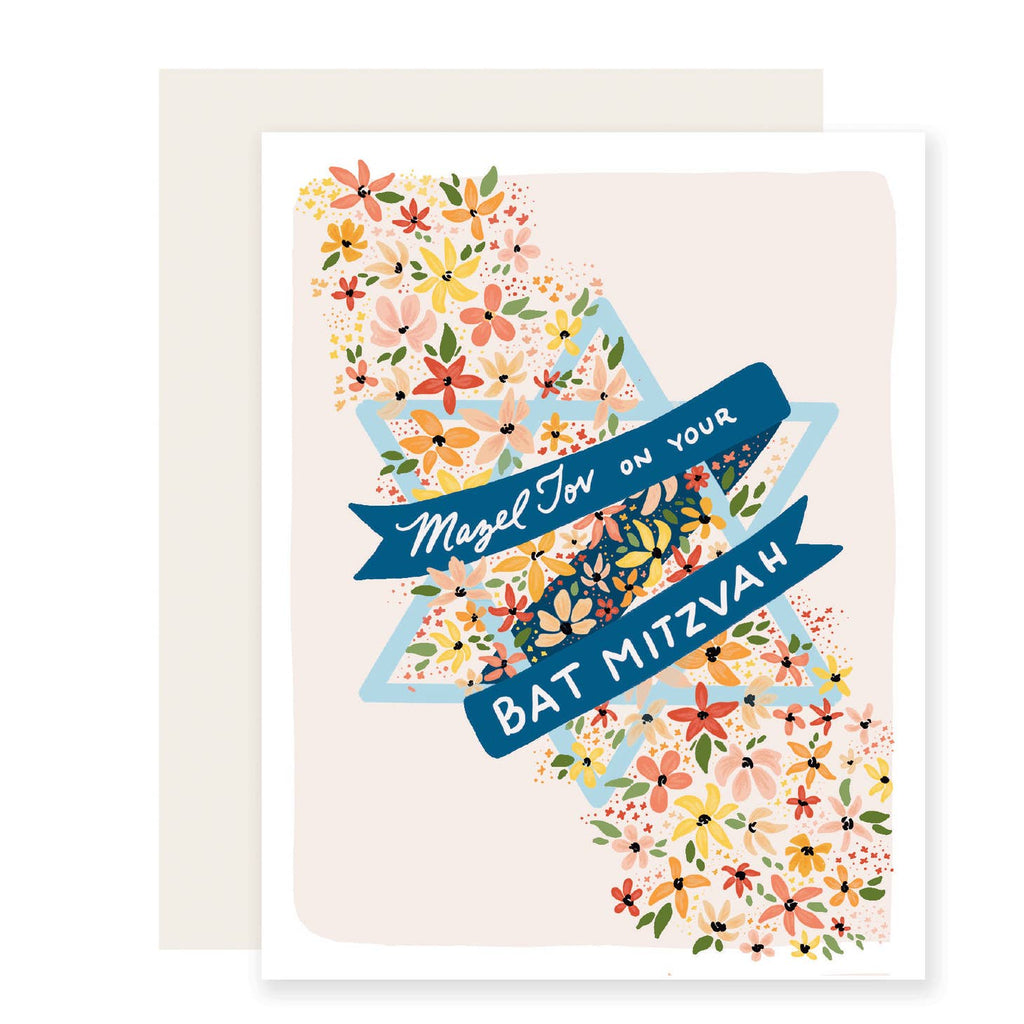 Light pink card with white text saying, “Mazel Tov on Your Bat Mitzvah!” Images of a blue Star of David and a diagonal row of orange, pink and yellow flowers across the card.  An ivory envelope is included.