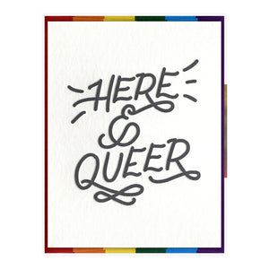 White card with black text saying, “Here & Queer”. A rainbow striped envelope is included.